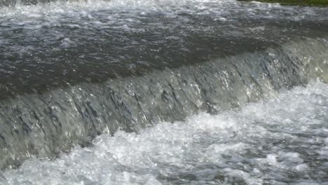 splashing water flows over a small artificial cascade waterfall closeup angle view