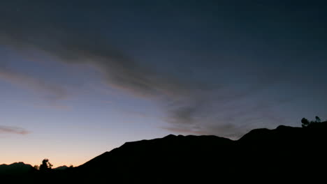 clouds move over a silhouetted mountain during golden hour