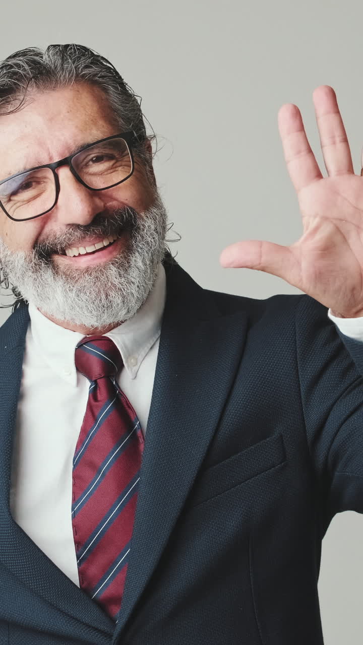 Uomo d'affari maturo sorridente che saluta con la mano in studio.