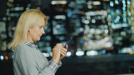 una mujer joven usa un teléfono inteligente en el fondo de las luces de la ciudad nocturna nueva york usa