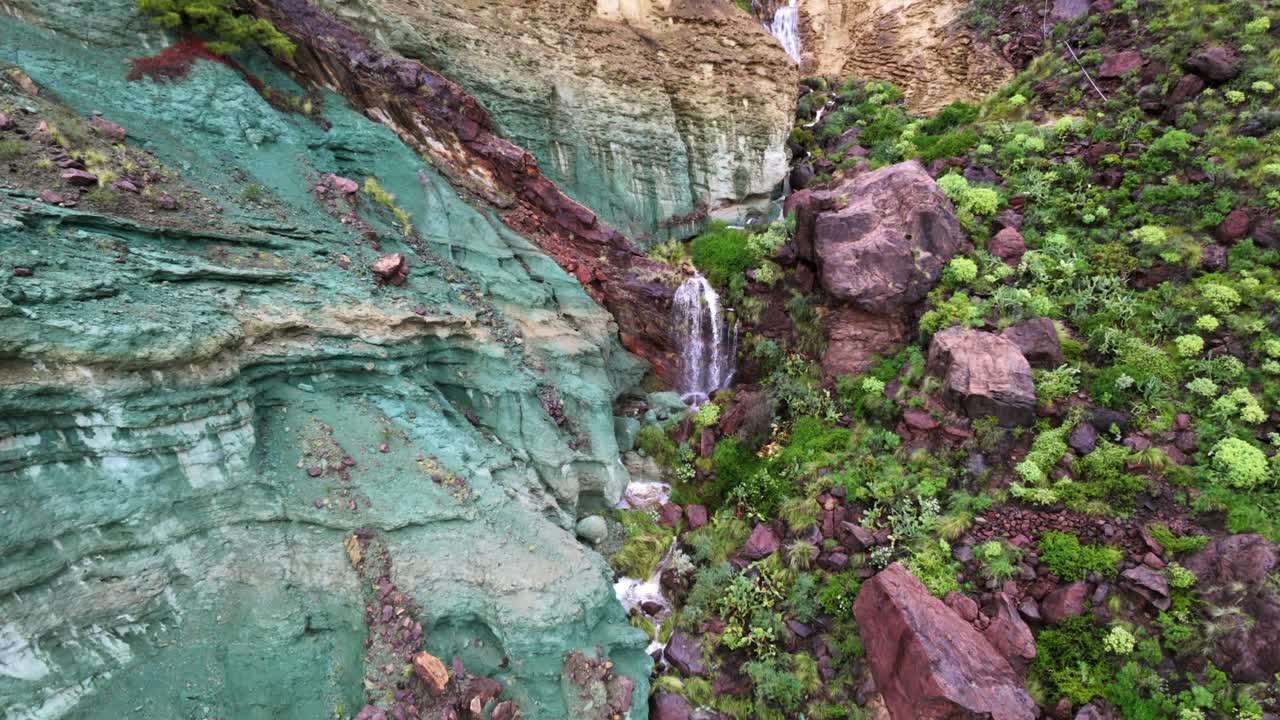 Formasi batuan berwarna-warni Los Azulejos de Veneguera di Mogan, Gran Canaria. Air terjun indah mengalir menuruni jurang setelah badai.