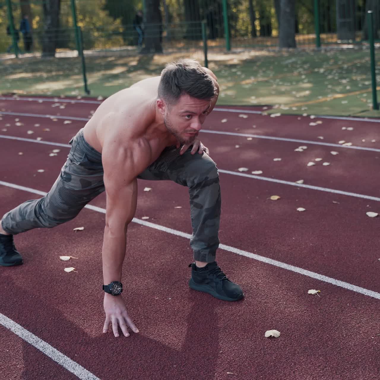 Shirtless athlete starts running on the stadium. Muscular male sprinter training on the outdoor athletics track. Sport and fitness concept.