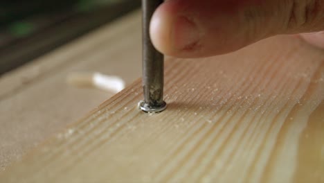 a macro shot of carpenter unscrewing a screw from a piece wood in slow motion