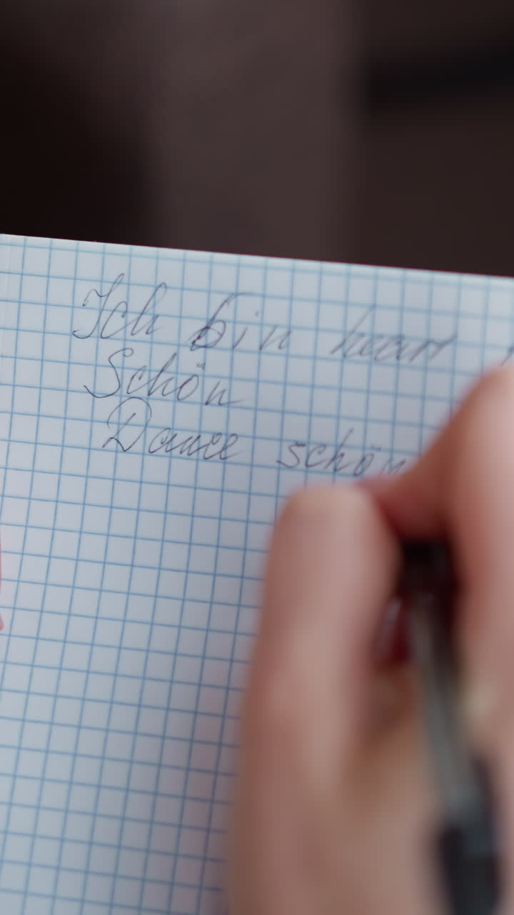Close-up hand view of individual writing in notebook with pen, showing graceful hand movements on graph paper, capturing details of handwriting process
