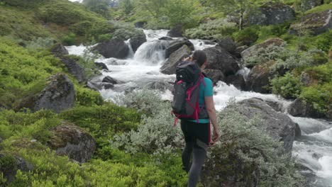 a woman - hiker with a backpack standing on the stone near a powerful and noisy water stream