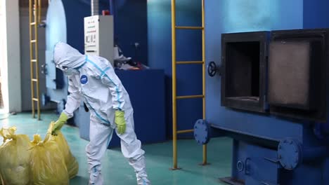 los trabajadores están cargando basura en el incinerador usando ropa protectora completa con máscaras