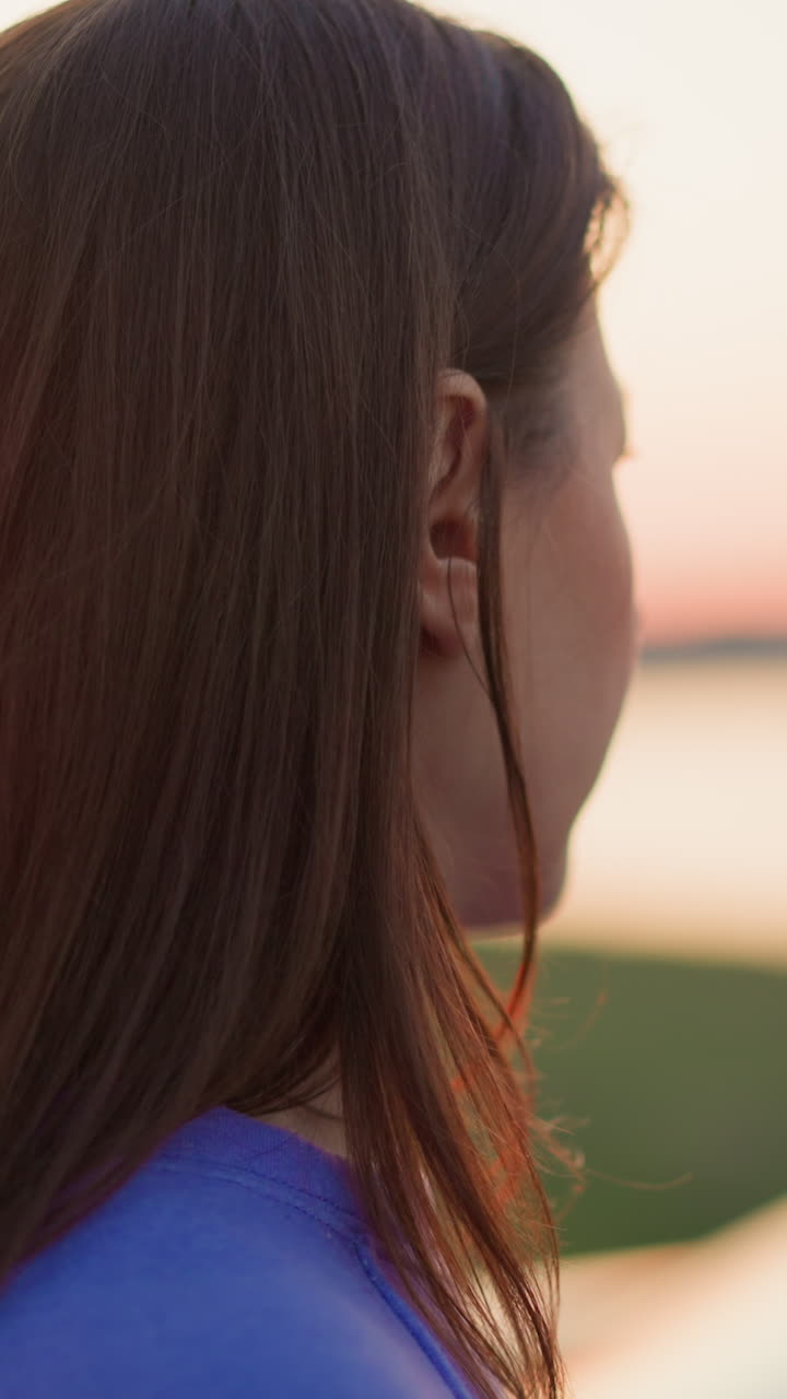 은 갈색 머리카락을 가진 조용한 여자가 황혼의 빛에서 강변을 상합니다. 여성 관광 농촌 휴가