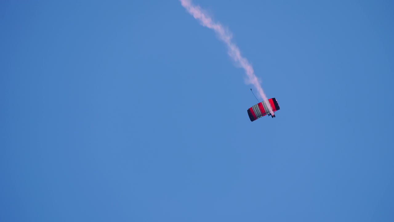 Aerobat faldskærmsudspringer med røgspor på klar blå himmel