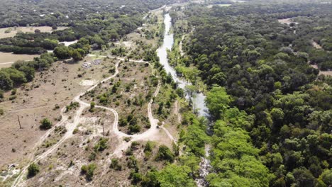 Comenzando-Por-Encima-Del-área-Del-Río-Muy-Sombreada-Por-Cipreses,-Volando-Hacia-Un-Campo-Grande-Con-Caminos-A-La-Izquierda---Gran-Extensión-De-árboles-A-La-Derecha---Imágenes-Aéreas-Del-Río-Blanco---Wimberly,-Tx