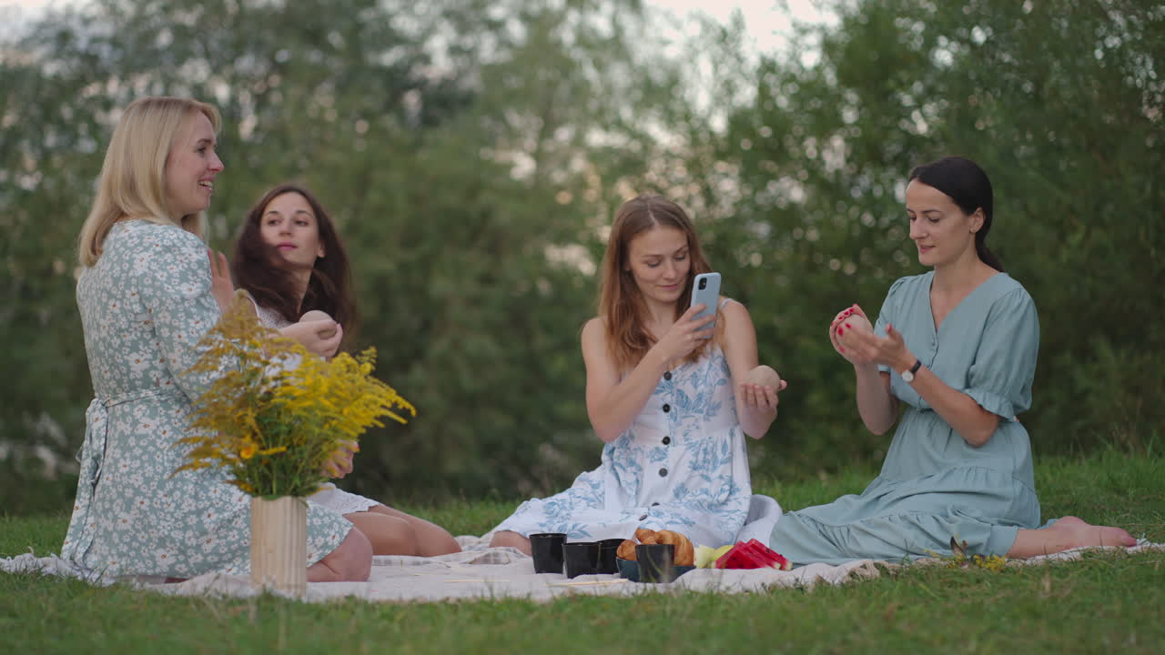 Young women in the open air conduct a clay modeling class. A lady takes pictures of the process on a phone smartphone takes a photo. Communication hobbies women's circle creative activity.