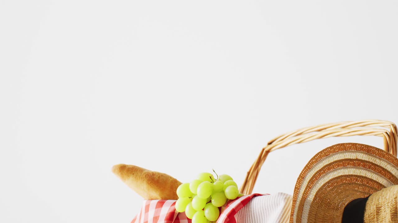cesta de picnic con manta a cuadros, uvas, baguette y sombrero sobre fondo blanco con espacio de copia