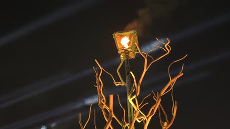 light show laser beam blue yellow design and a lantern with fire flame shining on top of a dry tree in a music festival provided food dj drink dance for tourists come to qatar dubai middle east