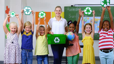 school kids and teacher holding recycling symbols and globe in classroom