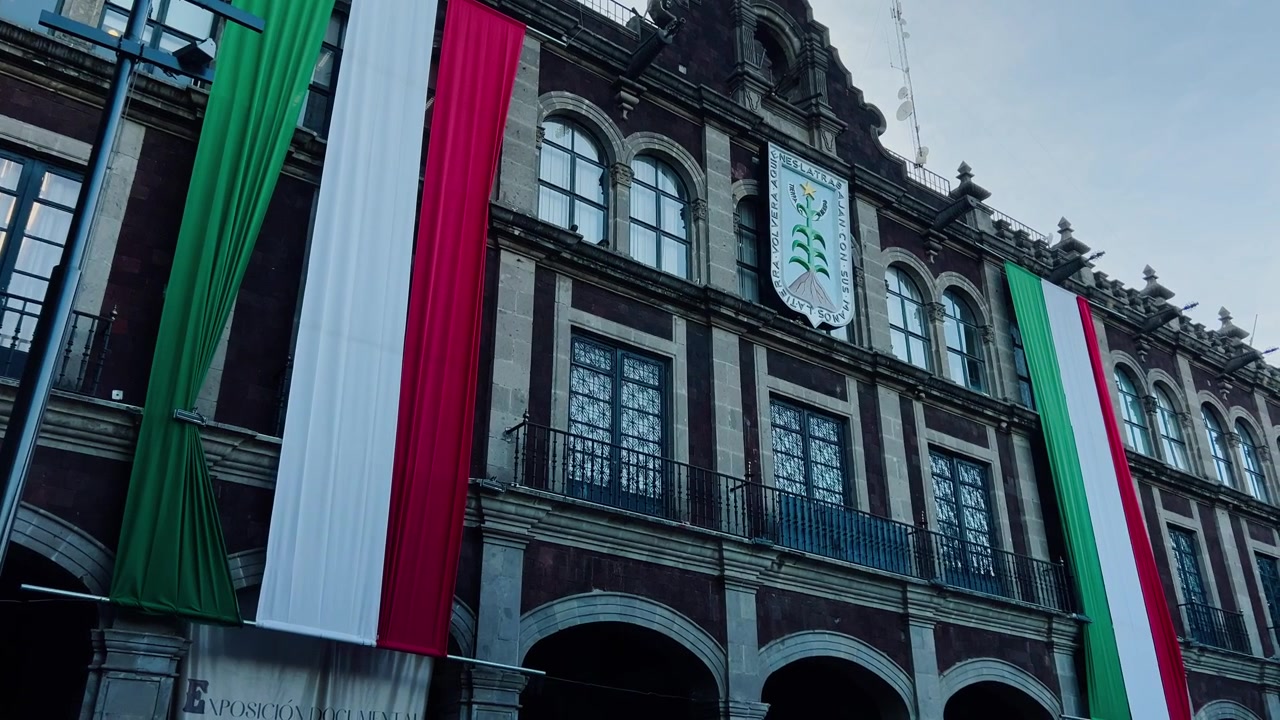 Edificio governativo storico messicano che espone grandi bandiere nazionali verdi, bianche e rosse, con facciata in pietra ornata, finestre ad arco e dettagli decorativi in Messico