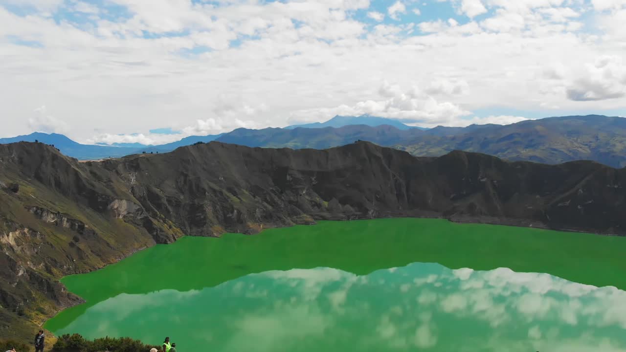 Aerial Drone Shot Reveals the Turquoise Crater of Quilotoa Lake with Tilt Down View and Tourists Gather Along the Crater's Edge in Awe