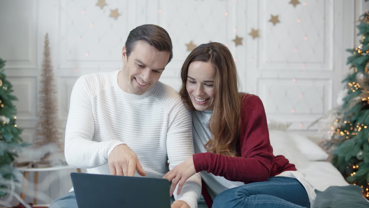 una pareja relajada buscando regalos de navidad en una computadora en un apartamento moderno.
