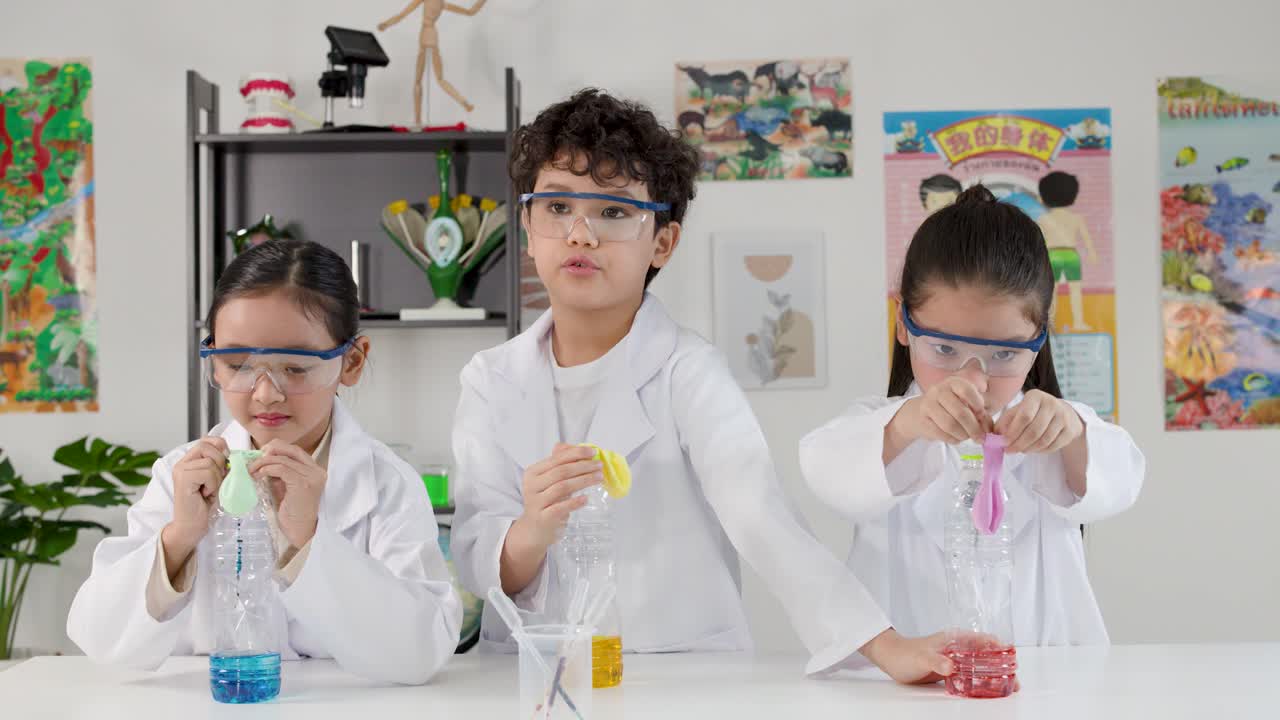 Asiatiske studerende i laboratoriekåber udfører et kemisk reaktionseksperiment ved hjælp af flasker og balloner.