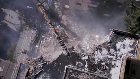 Aerial-shot-of-an-excavator-demolishing-a-building,-dust-rising