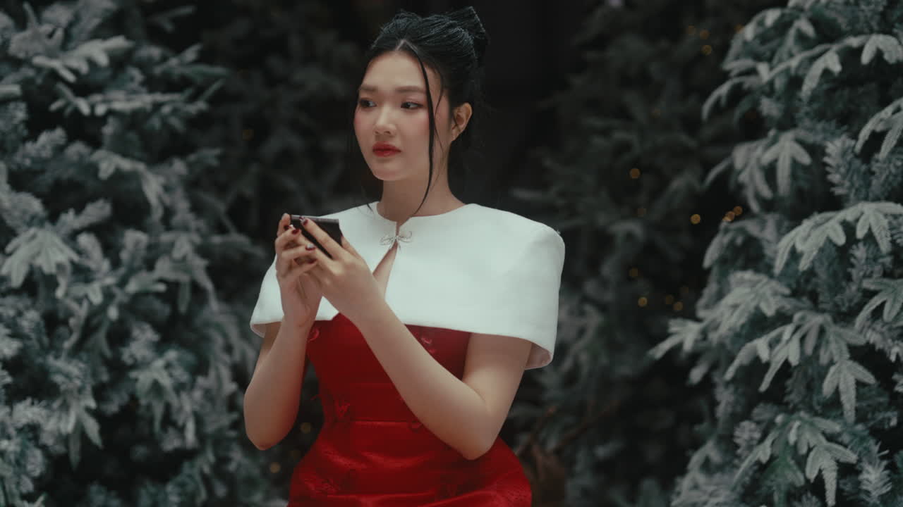 A woman in a red dress holds a phone, looking worried in a snowy forest setting