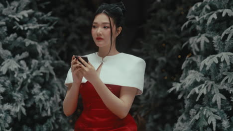 a woman in a red dress holds a phone, looking worried in a snowy forest setting