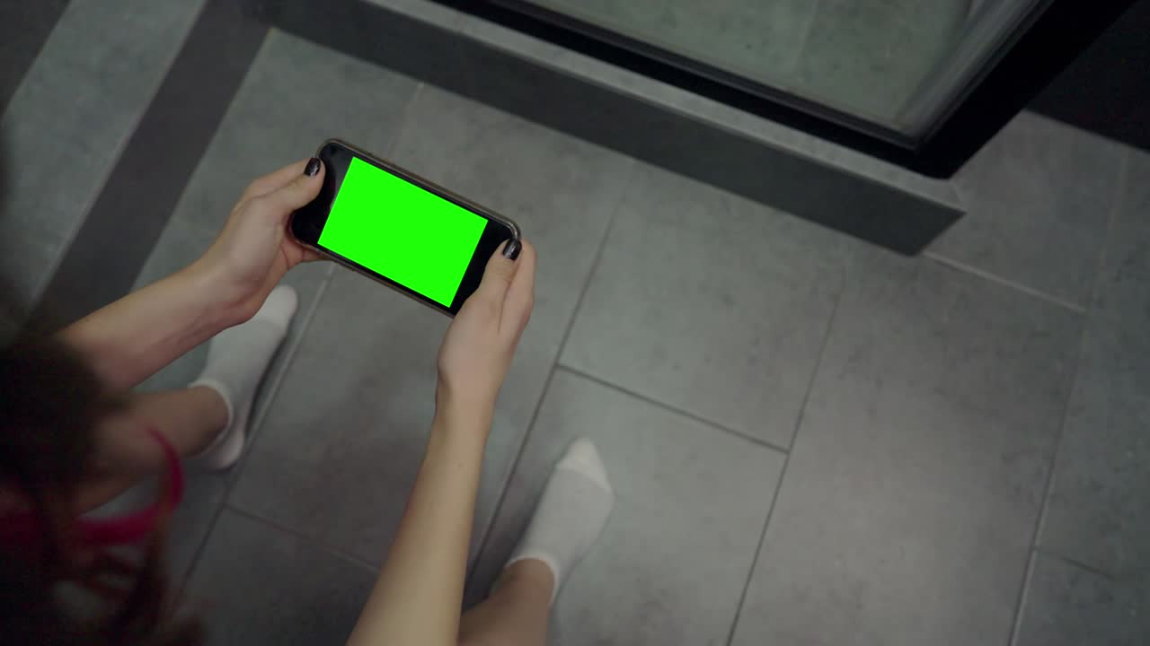 Giovane donna seduta sul WC che guarda contenuti multimediali sul suo cellulare