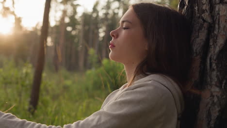 woman thinks with closed eyes leaning on tree trunk at sunset. depressed lady considering psychology help to cope with stress in calm atmosphere of evening in nature