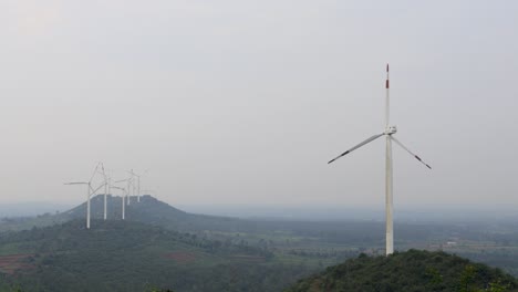 a awesome view of a hill range with a few modern windmills seen generating wind energy with slow moving rotor blades near hassan city in karnataka, india.