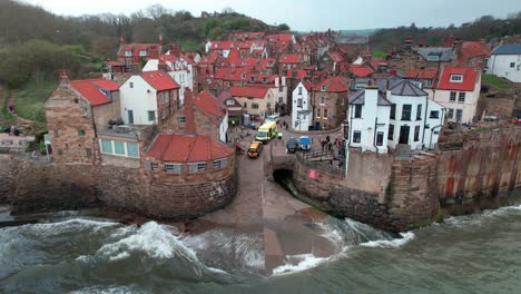 waves crashing against colourful robin's hood bay town houses static aerial view close up