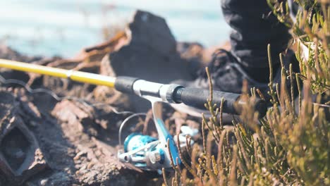 man's hand picks up fishing rod on shoreline