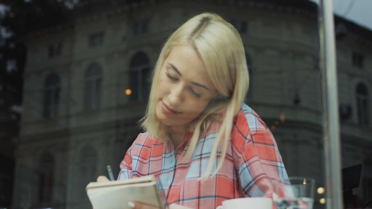 Blonde Woman Sitting In A Cafe And Thinking While Writing Something With A Pencil In Her Notebook