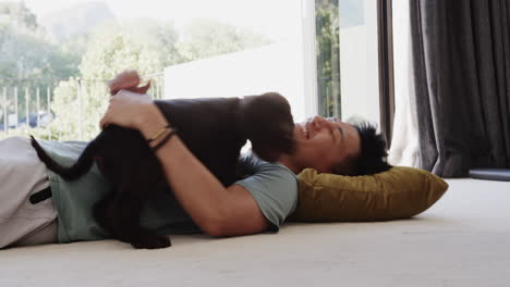 asian man laughing while playing with dog on floor at home