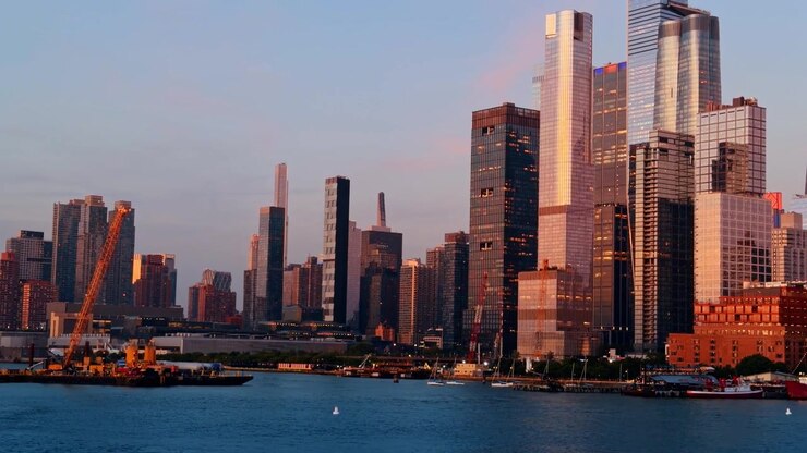 Torres de Hudson Yards ao lado do Rio Hudson ao pôr do sol, barcaça de construção, veleiros e fachadas refletivas