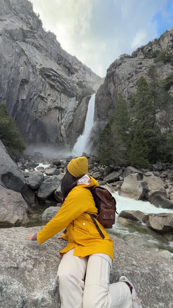 Mujer feliz posando junto a una majestuosa cascada en un paisaje montañoso
