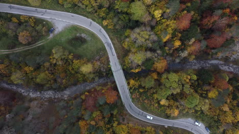 Imágenes-Aéreas-De-Un-Coche-Blanco-Cruzando-El-Puente-Sobre-El-Río-En-El-Bosque-Montañoso-De-Los-Pirineos-En-Otoño-En-El-Norte-De-España-Durante-La-Hermosa-Puesta-De-Sol