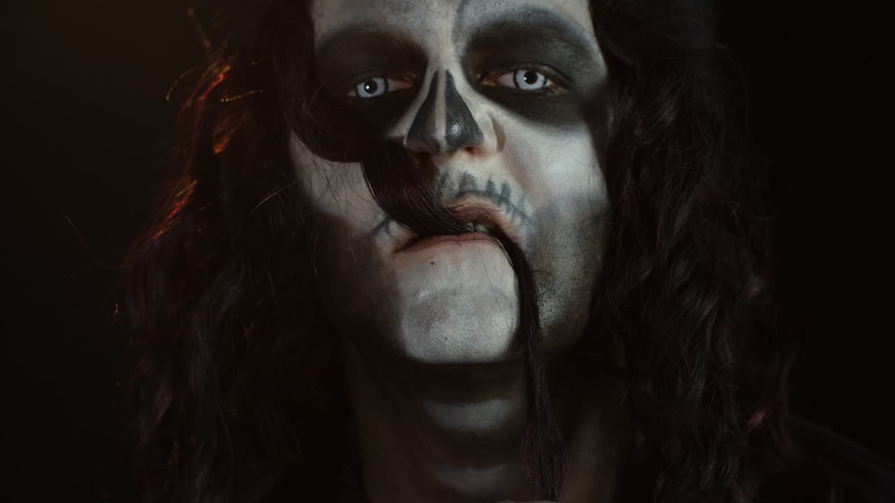 Creepy long hair man with skeleton makeup making faces and pointing at camera, trying to scare