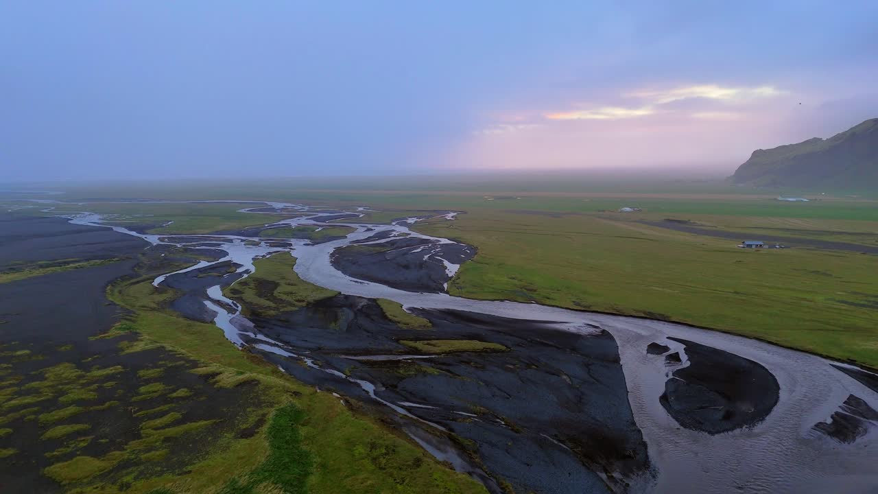 Icelandic streams twist on their journey through glaciated valleys, volcanic rock and vibrant mossy green flatlands to the sea. Drone aerial reveal horizon