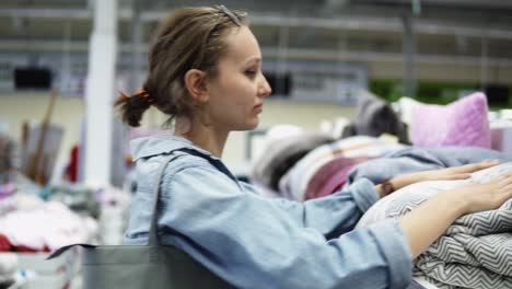 a young positive fair-haired girl chooses pillows and a blanket on the racks in the store. touches, checks the quality. playfully take a nap on a pillow. supermarket