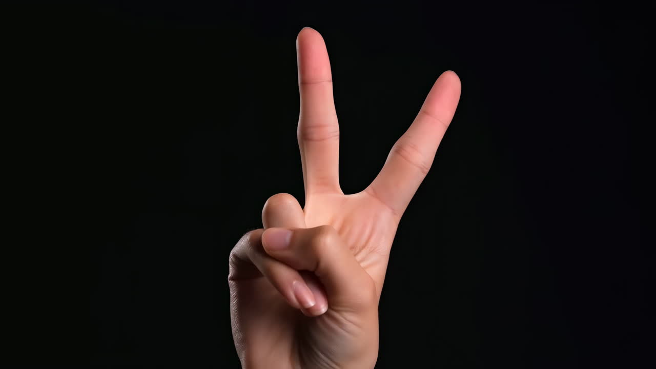 Primo piano di una mano che mostra il segno della pace su sfondo nero, vista ravvicinata illuminata da studio di due dita alzate che formano il segno V