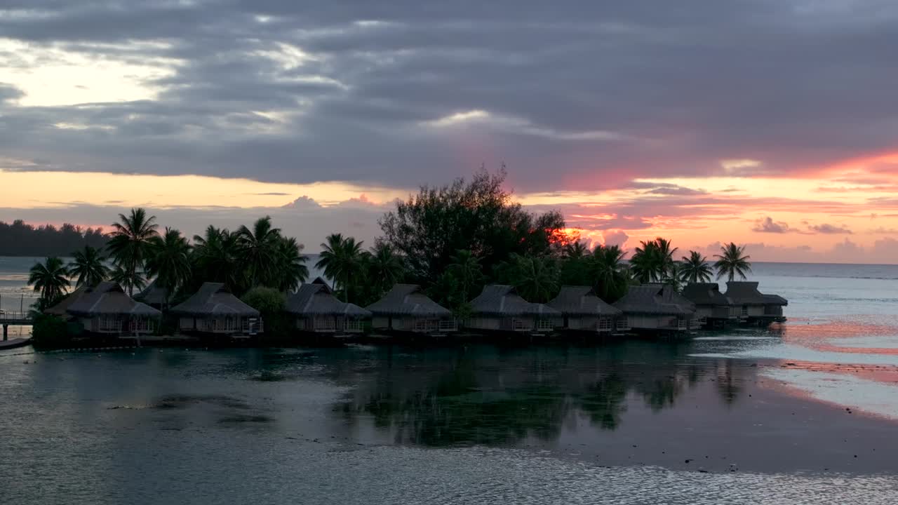 Stunning vibrant pink orange sunset sun rays Sofitel Kia Ora Resort Bungalow villas Moorea island French Polynesia aerial drone Cooks Opunohu Bay lagoon coral reef Pacific Ocean upward jib motion