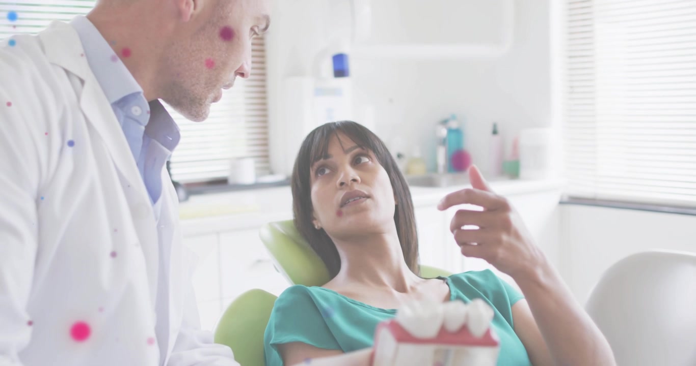 Dentista pegando modelo dental explicando a escovação enquanto paciente gira o modelo sob uma sobreposição colorida