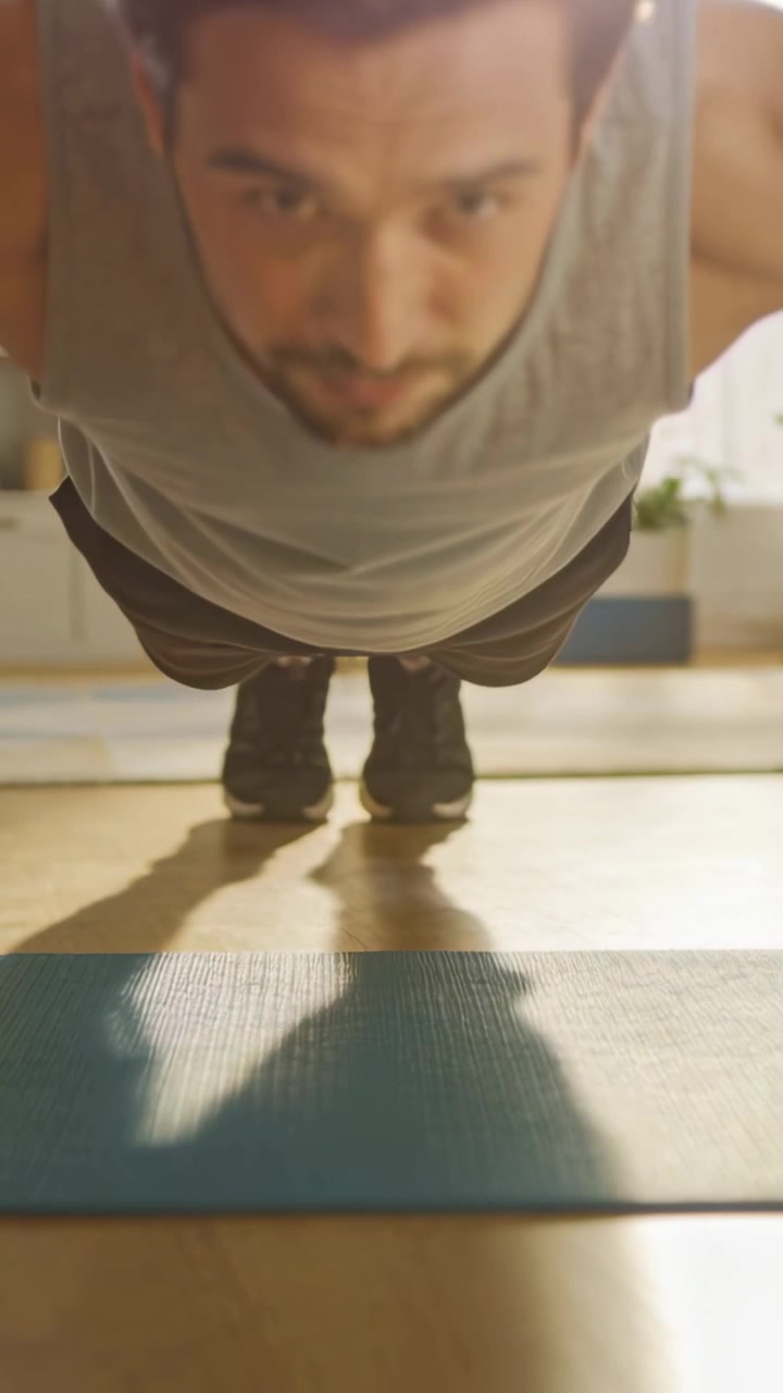 Video verticale: Uomo indiano in canotta che inizia il plank, abbassandosi e spingendosi su un tappetino per un allenamento a casa