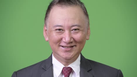 mature happy japanese businessman smiling against green background