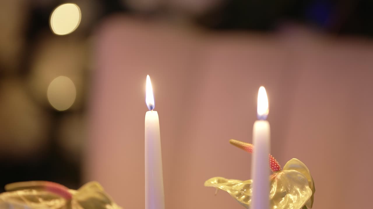 Two white candles burning gently with floral decor in warm low light atmosphere
