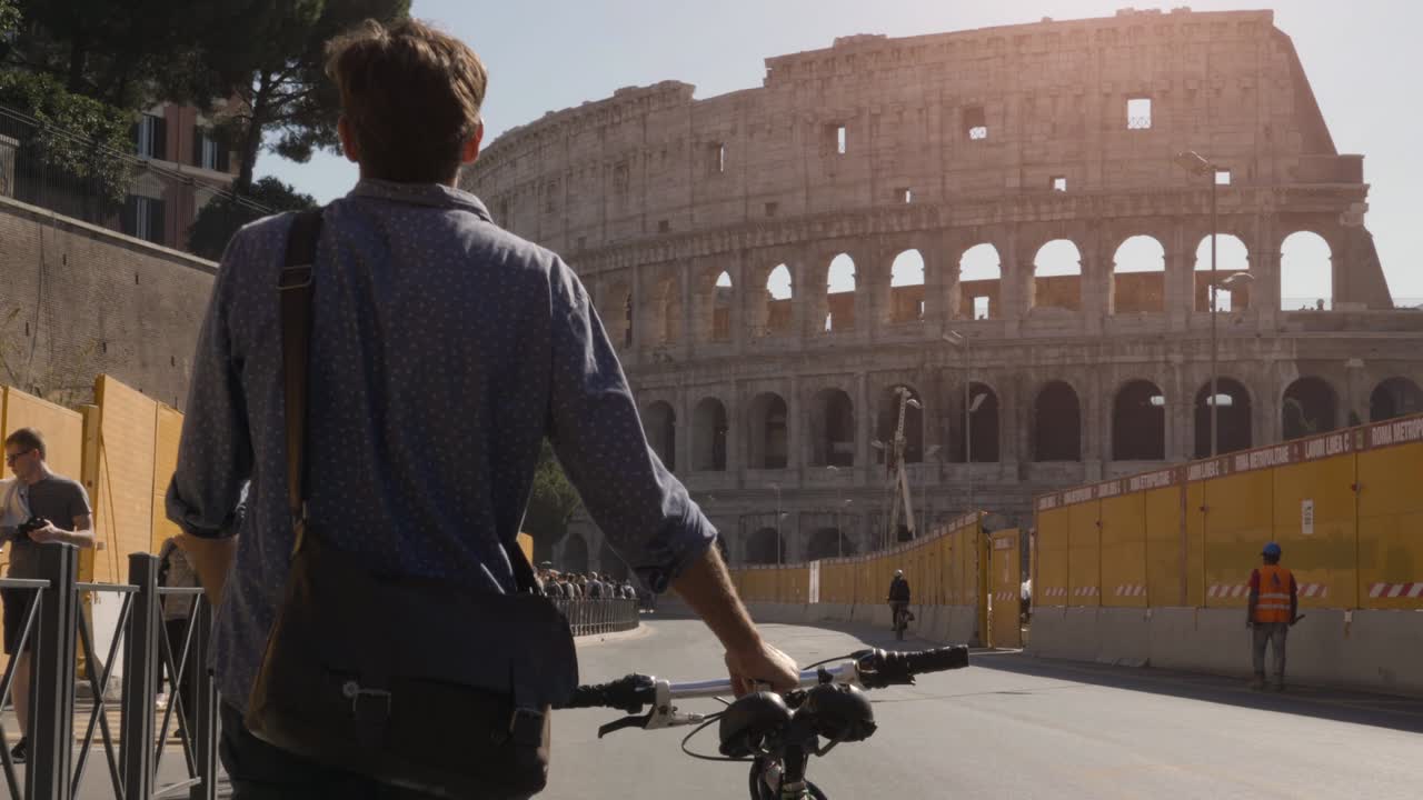 젊은 스터 남자가 로마 포럼에서 자전거를 타고 로마 시내 중심의 콜로세움으로 향하고 있습니다.