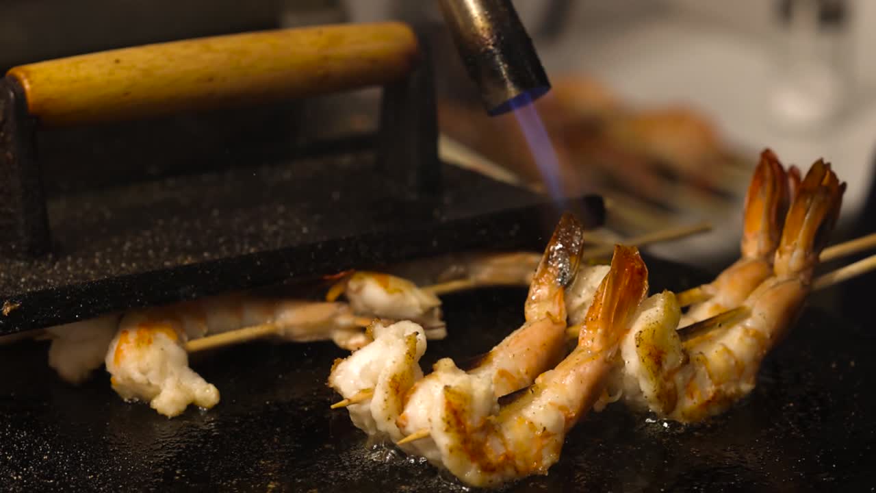 Close-up of shrimp being seared with a torch on a grill press.