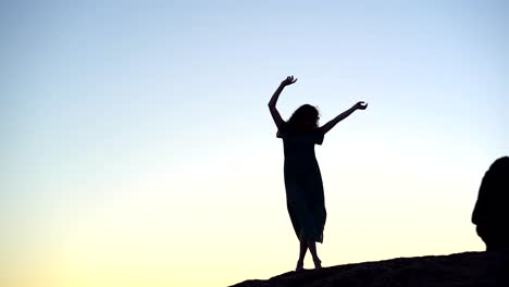 female silhouette standing gracefully with arms raised on hilltop