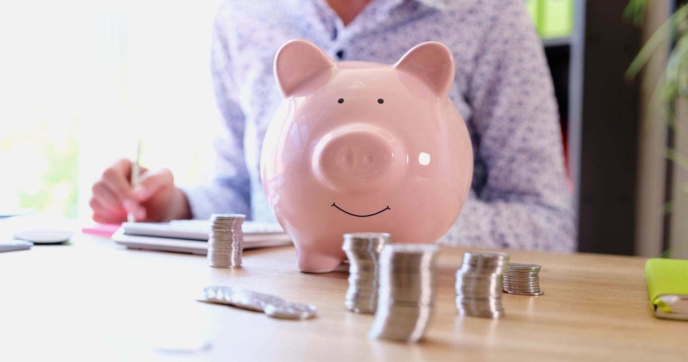 Disfrutando el momento de ahorro con una alcancía feliz y monedas cuidadosamente apiladas en un espacio de trabajo soleado