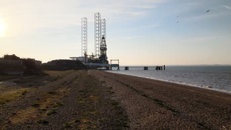 Filmische-Low-Level-Antenne-über-Dem-Strand-Von-Sheerness-Kent-In-Richtung-Einer-Nordsee-Bohrinsel,-Die-Gewartet-Wird