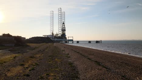cinematic low-level aerial over the beach at sheerness kent towards a north sea oil rig undergoing maintenance