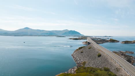 aerial view of a boat sailing under storseisundet bridge on atlantic road also known as ”the road in the ocean” in norway